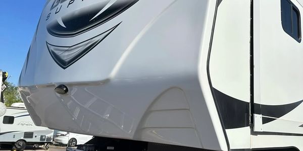 White Genesis Supreme fifth-wheel RV parked under a clear blue sky.