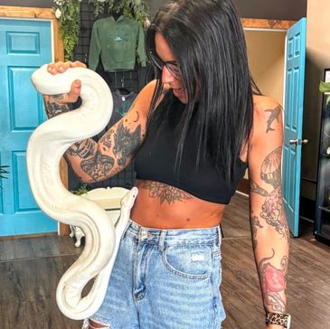 A tattooed woman holding a white snake indoors.