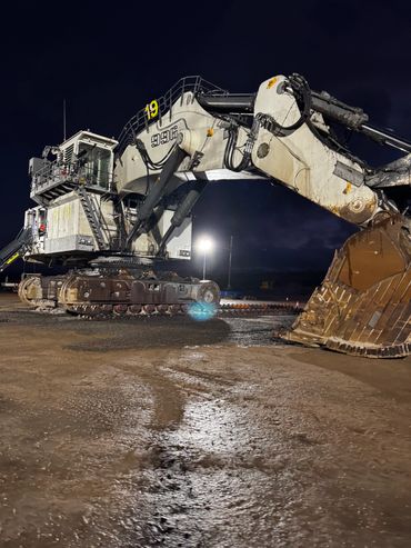 Large excavator machine illuminated at night on muddy ground.
