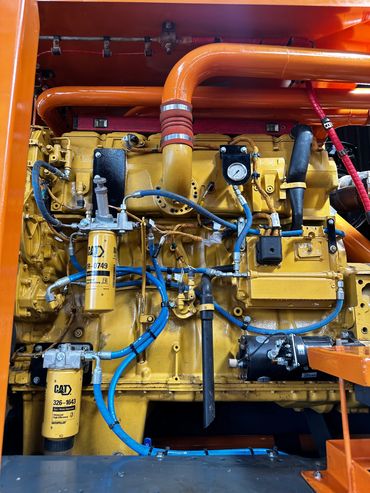 Close-up of a yellow Caterpillar engine with blue hoses and orange pipes.