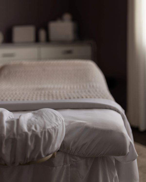 Cozy massage table with white linens and beige blanket.