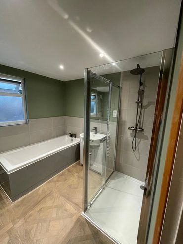 Modern bathroom with a glass shower, bathtub, and sink in muted green and neutral tones.