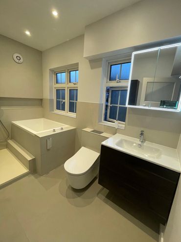 Modern bathroom with bathtub, wall-mounted toilet, and illuminated mirror.