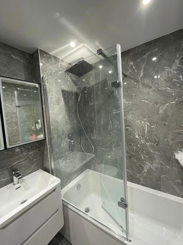 Modern bathroom with marble walls, glass shower screen, and white vanity sink.
