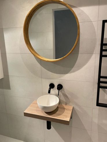 Minimalist bathroom sink with round wooden mirror and matte black fixtures.