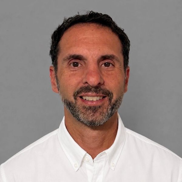 Man with short dark hair and beard wearing a white button-up shirt.