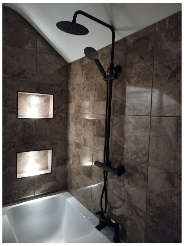 Elegant bathroom installation comprising a mixture of brown tiles, niche lighting & black faucets.