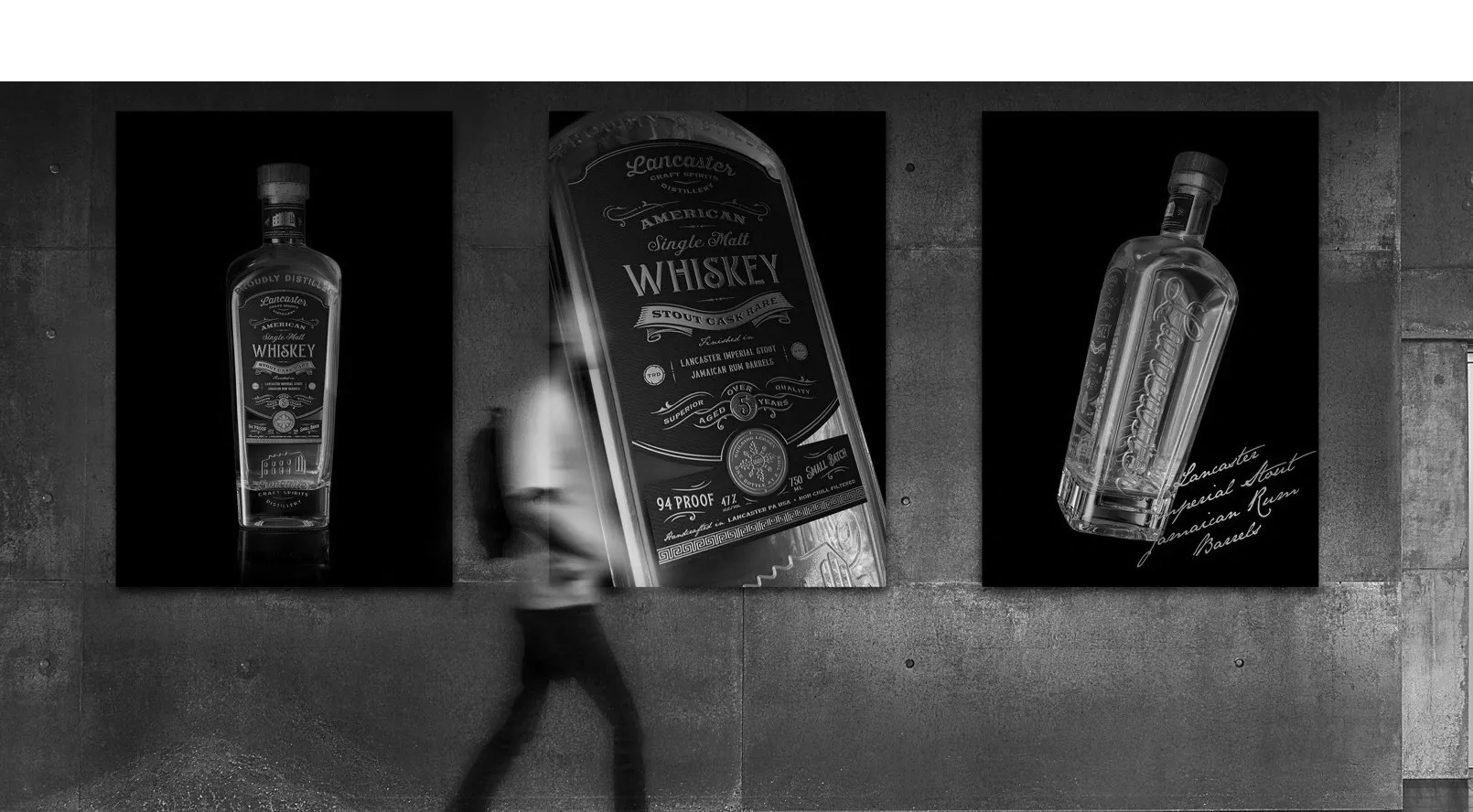 Three posters of Lancaster American Single Malt Whiskey displayed on a concrete wall.