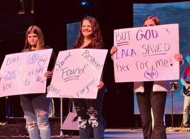 Mom holding cardboard testimony with daughters, sharing her story of surviving a fentanyl overdose.