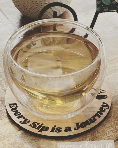 Glass cup of tea on a coaster with the phrase 'Every sip is a journey'.