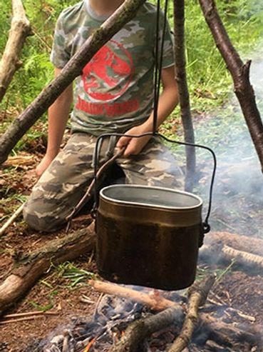 Kids cooking over a campfire in the woods.