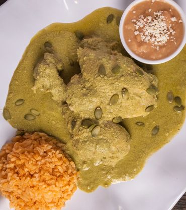 Traditional Mexican mole verde dish with rice and tortillas.