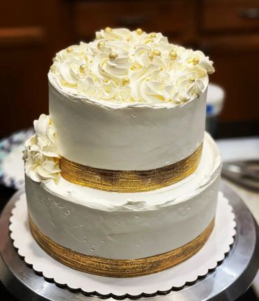 Elegant two-tier white cake with gold ribbon and cream swirls.