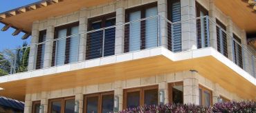 Horizontal cable railing wraps around a stone-clad balcony beneath a timber soffit.