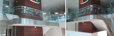 Curved glass railing, round metal handrail and wide metal fascia at an atrium landing.