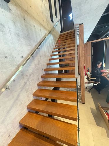 Wood treads, glass guardrail and central steel stair support in a bright interior.