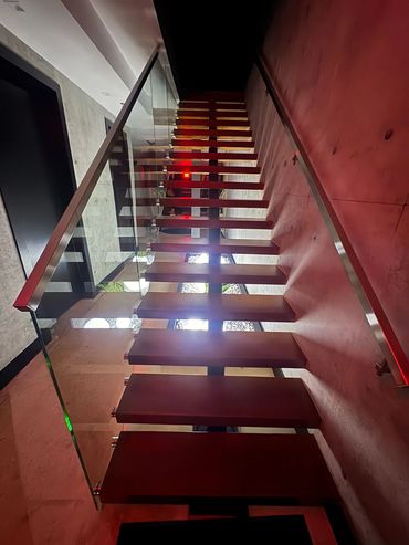 Upward view of wood stair treads, glass balustrade and metal handrails beside concrete walls.