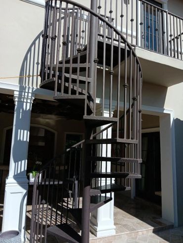Painted exterior spiral stair with diamond-plate treads and decorative vertical metal balusters.