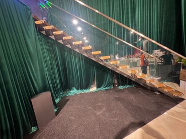 Wood-tread floating stair with steel support and glass balustrade; venue setup behind.