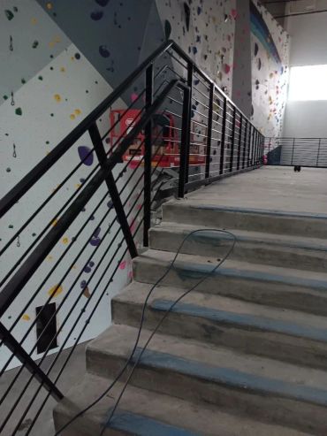 Black guardrails beside concrete steps in a climbing facility with construction tools visible.