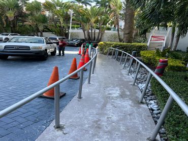 Round metal handrails follow a curved walkway, with cones and site crew indicating installation.