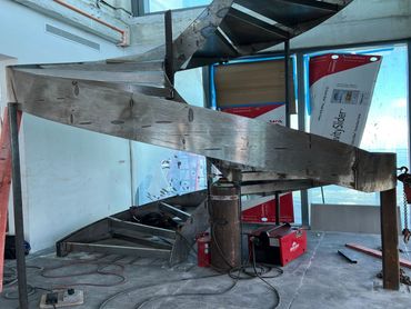 Curved steel stair stringer and metal treads during fabrication, with welding equipment.