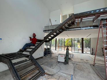 Steel stair framework during installation, with workers, ladders and welding tools.