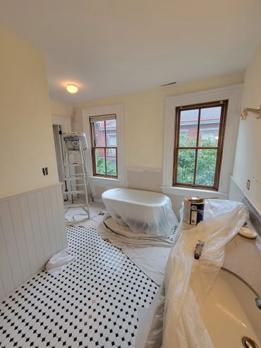 Bathroom under renovation with plastic-covered tub and painting supplies.