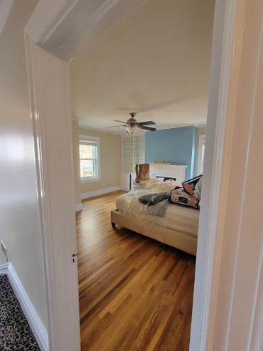 View into a bedroom with wooden floor, ceiling fan, and some packed items on the bed.