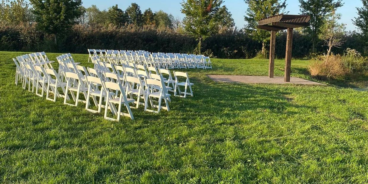 White chairs arranged outdoors for an event near a wooden pergola.
