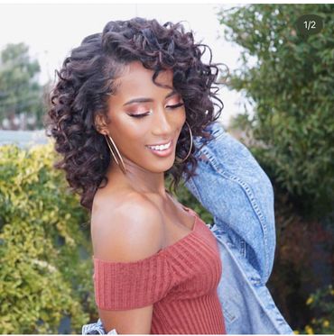Smiling woman with curly hair wearing a rust-colored off-shoulder top and denim jacket.