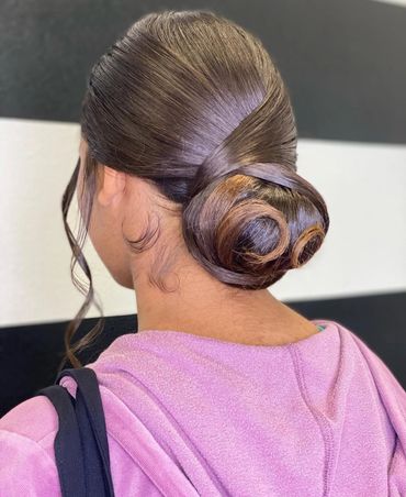 Elegant low bun hairstyle with smooth, shiny hair and curled strands framing the face.