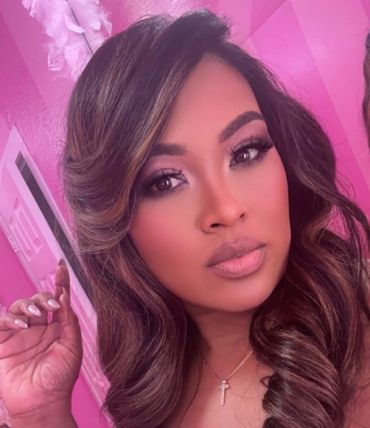 Woman with styled hair and makeup posing against a pink wall.