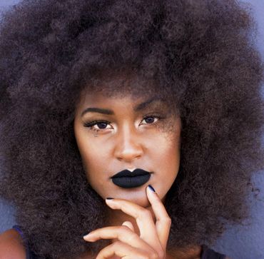 Close-up of a woman with voluminous curly hair and bold black lipstick.