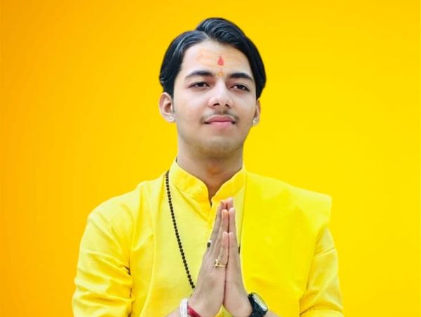 Young man in yellow traditional attire with hands joined in namaste gesture.