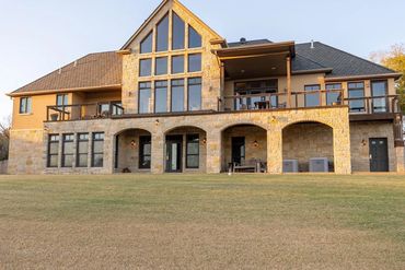 Large modern stone house with expansive windows and a spacious lawn.