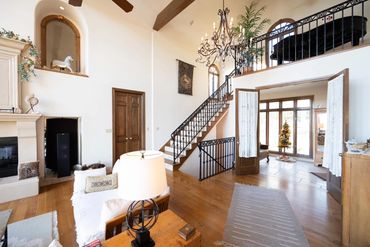 Spacious living area with wooden stairs, chandelier, and Christmas tree in adjoining room.