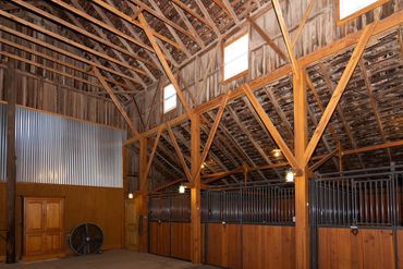 Interior of a clean, wooden horse stable with metal bars and high ceilings.