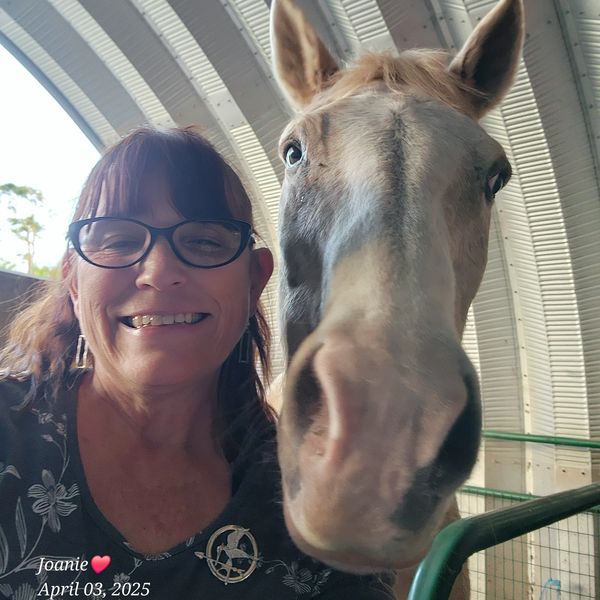 Woman smiling with a close-up horse inside a barn.
