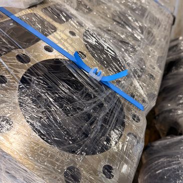 Metal engine part wrapped in plastic with a blue tie strap.