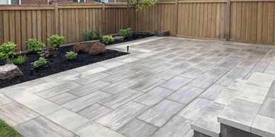 A modern backyard patio with large gray tiles and a wooden fence.