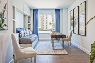 Modern home office with blue and neutral tones, featuring a desk, chairs, and a daybed by a large window.