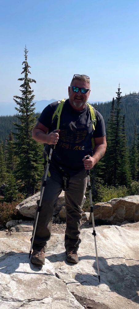 Man hiking with trekking poles in a forested mountain area.