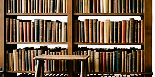 Vintage bookshelves filled with old books and a wooden stool.