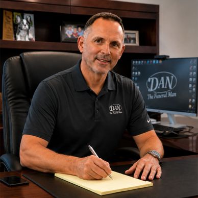 Man in black polo shirt sitting at desk, writing in a notepad.