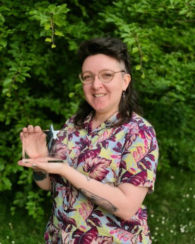 Emma Denny stands in a park holding the RNA's Popular Romance Award.