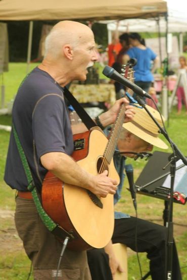 Man passionately singing and playing guitar at an outdoor event.