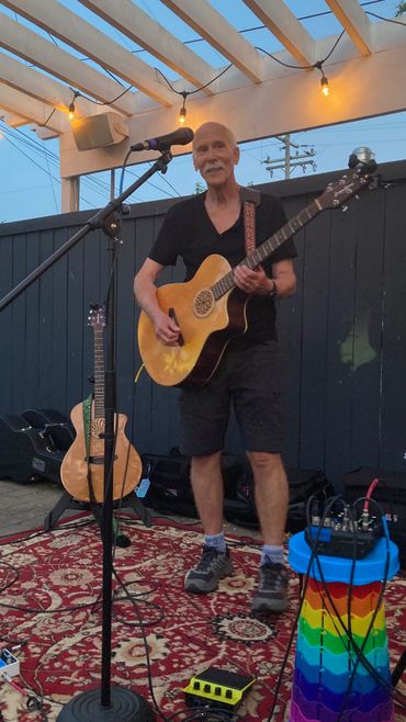 Man playing acoustic guitar during an outdoor performance at dusk.