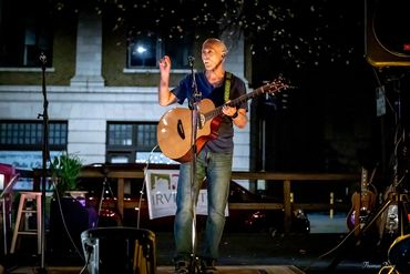 Man playing guitar and singing on an outdoor night stage.