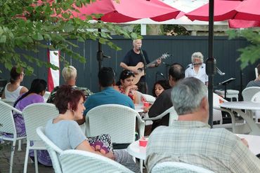 People enjoy live music outside under red umbrellas at a cafe.